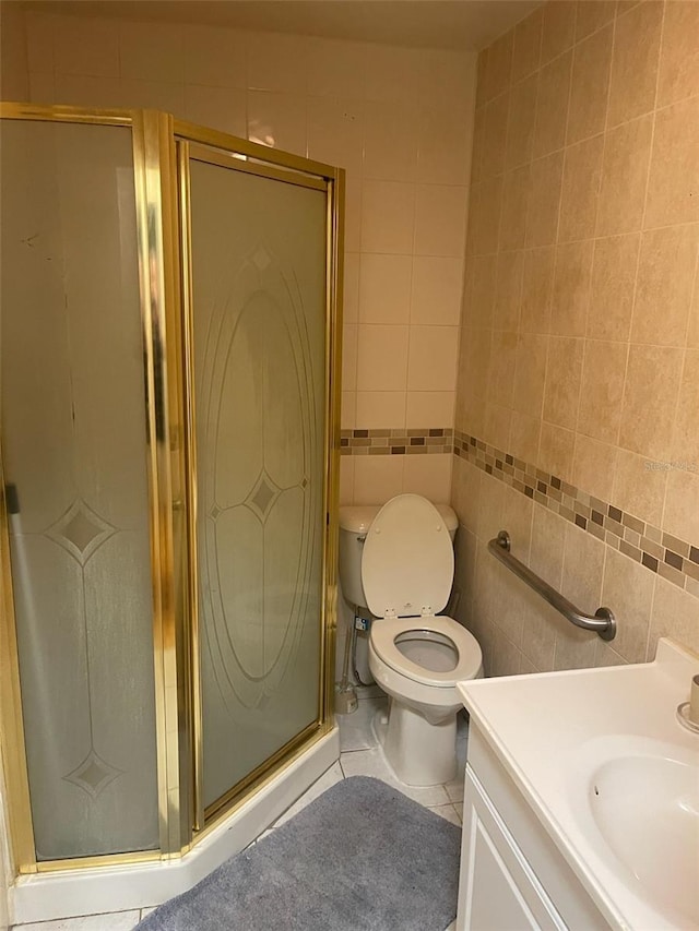 bathroom featuring tile patterned flooring, toilet, vanity, a shower with shower door, and tile walls