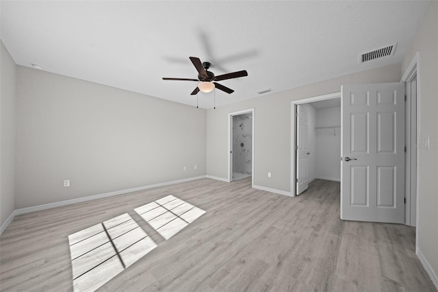 unfurnished bedroom featuring light hardwood / wood-style flooring, ceiling fan, a spacious closet, connected bathroom, and a closet