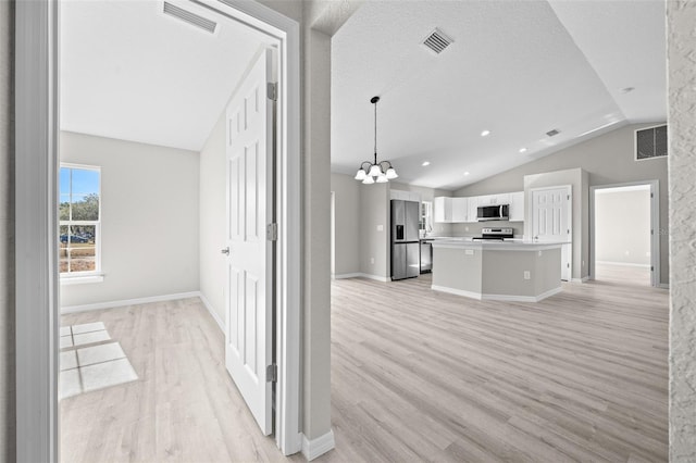 kitchen featuring stainless steel appliances, vaulted ceiling, pendant lighting, white cabinets, and a kitchen island