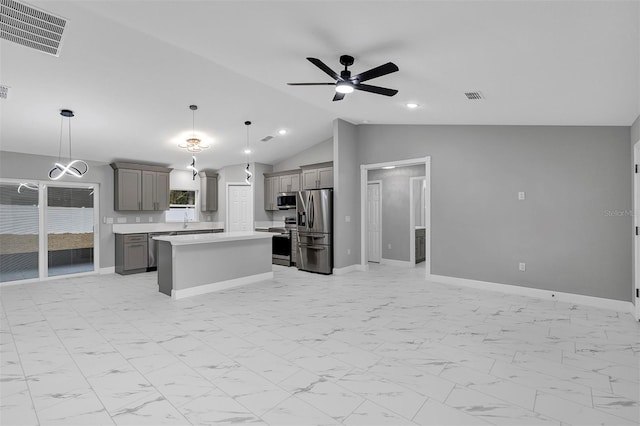 kitchen with lofted ceiling, ceiling fan, appliances with stainless steel finishes, decorative light fixtures, and a kitchen island