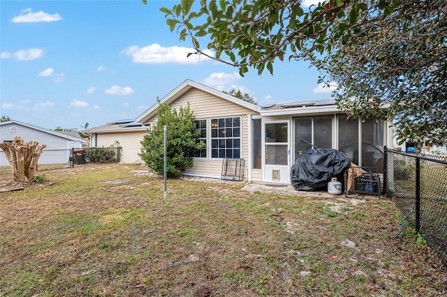 rear view of property with a sunroom, a fenced backyard, a yard, and solar panels