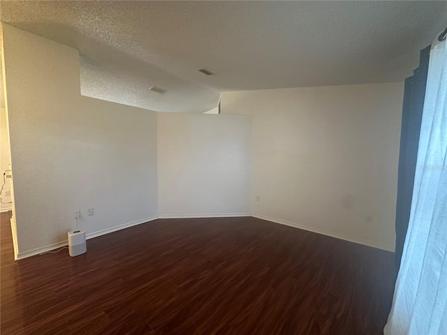 unfurnished room with dark wood-type flooring, a textured ceiling, and lofted ceiling