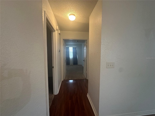 hallway with a textured wall, a textured ceiling, baseboards, and wood finished floors