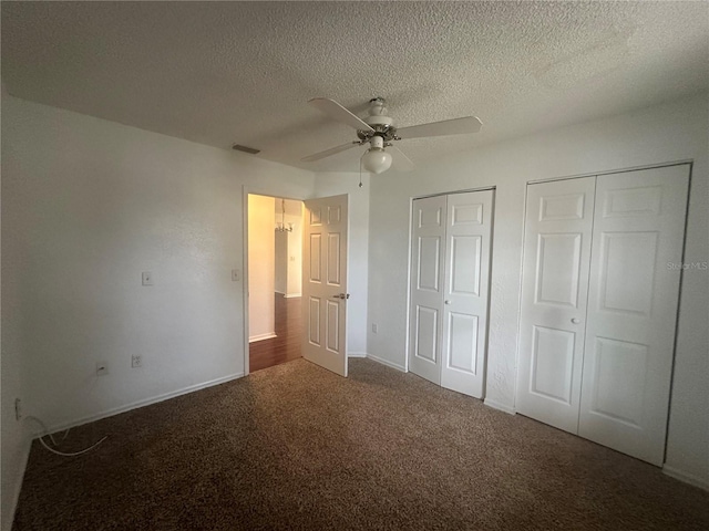 unfurnished bedroom featuring ceiling fan, a textured ceiling, dark colored carpet, and multiple closets