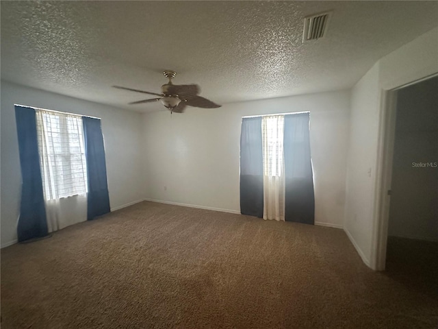 carpeted spare room featuring a ceiling fan, a healthy amount of sunlight, visible vents, and a textured ceiling