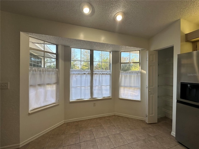 unfurnished dining area featuring tile patterned flooring, a textured ceiling, and baseboards