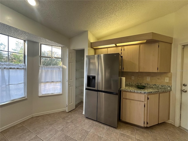 kitchen featuring lofted ceiling, light tile patterned floors, a textured ceiling, baseboards, and stainless steel fridge