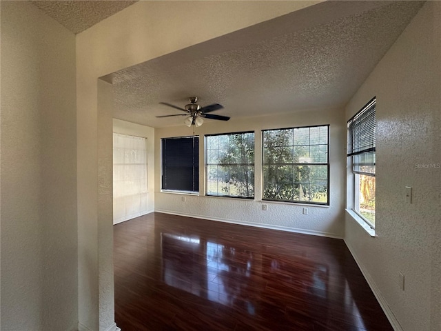 empty room with baseboards, dark wood finished floors, a ceiling fan, a textured wall, and a textured ceiling