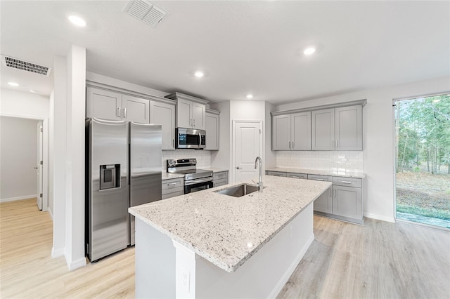 kitchen featuring a kitchen island with sink, sink, light stone countertops, light wood-type flooring, and stainless steel appliances