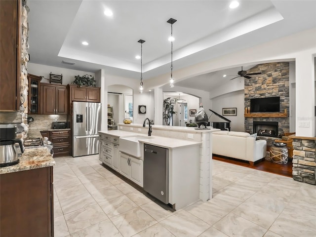 kitchen with a tray ceiling, sink, an island with sink, and appliances with stainless steel finishes