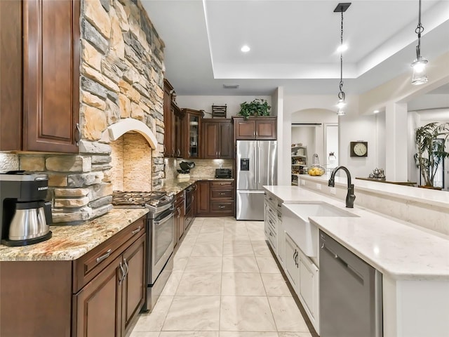 kitchen featuring sink, stainless steel appliances, decorative light fixtures, a tray ceiling, and decorative backsplash