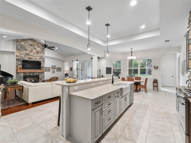 kitchen with sink, an island with sink, a kitchen bar, gray cabinets, and a fireplace