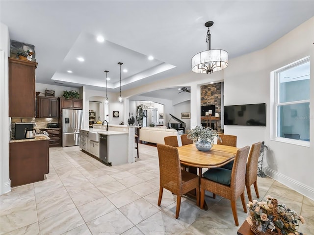 dining room featuring ceiling fan with notable chandelier, a tray ceiling, and sink