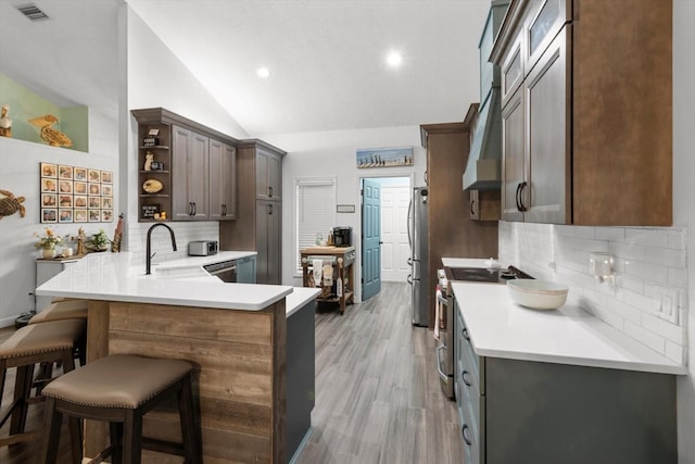 kitchen with kitchen peninsula, appliances with stainless steel finishes, sink, lofted ceiling, and a breakfast bar area