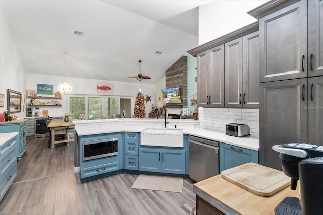 kitchen with sink, stainless steel appliances, kitchen peninsula, pendant lighting, and lofted ceiling