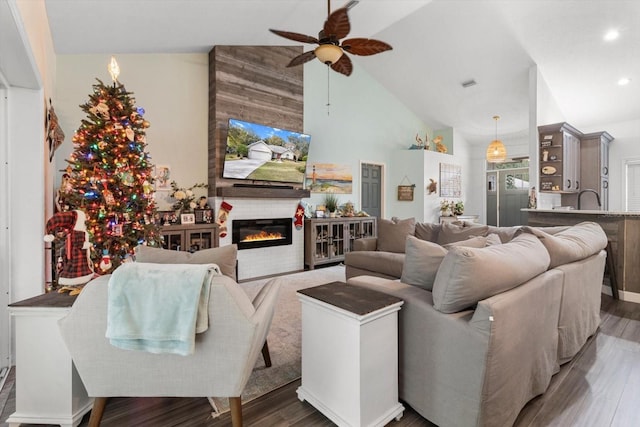 living room with a large fireplace, dark hardwood / wood-style floors, ceiling fan, and high vaulted ceiling