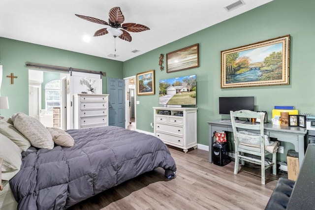 bedroom with ceiling fan, a barn door, and light hardwood / wood-style flooring