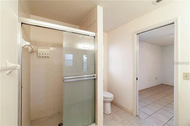 bathroom with tile patterned floors, toilet, a shower with door, and a textured ceiling