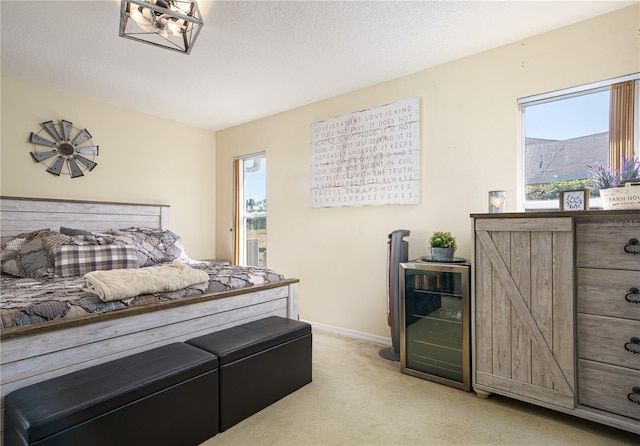 bedroom with light carpet, wine cooler, a textured ceiling, and baseboards