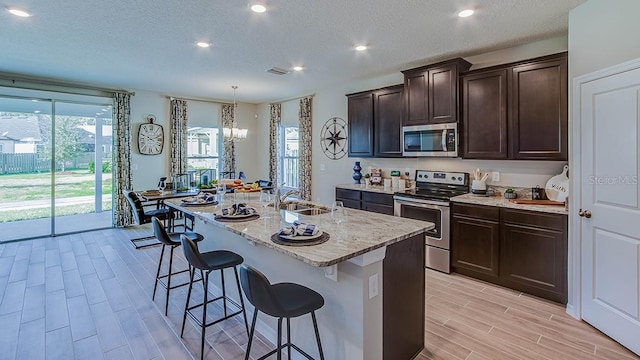 kitchen with sink, stainless steel appliances, a kitchen breakfast bar, a textured ceiling, and a kitchen island with sink