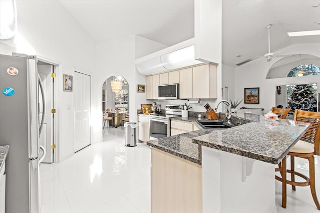 kitchen featuring sink, a kitchen breakfast bar, vaulted ceiling, light tile patterned flooring, and appliances with stainless steel finishes