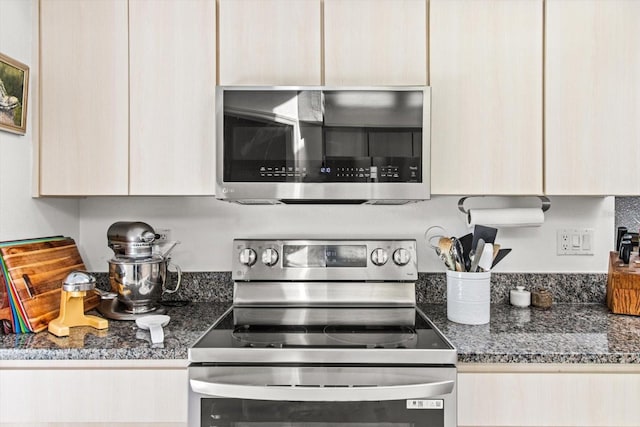 kitchen with light brown cabinetry, stainless steel appliances, and dark stone counters