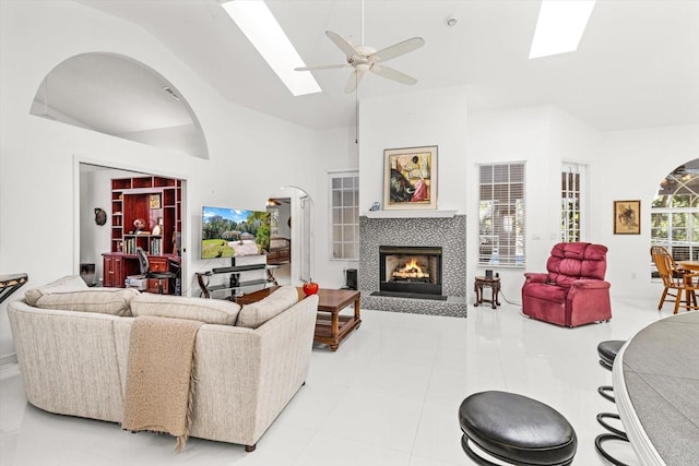 tiled living room featuring a skylight, ceiling fan, a fireplace, and a high ceiling