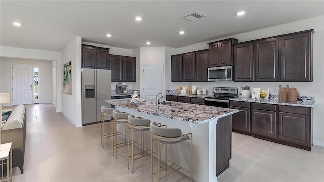 kitchen with a center island with sink, sink, appliances with stainless steel finishes, dark brown cabinetry, and a breakfast bar area