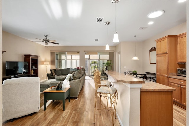 kitchen featuring a center island with sink, sink, hanging light fixtures, light hardwood / wood-style flooring, and ceiling fan