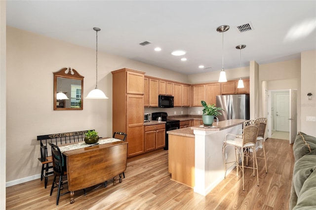 kitchen with a kitchen breakfast bar, light hardwood / wood-style flooring, pendant lighting, a kitchen island, and black appliances