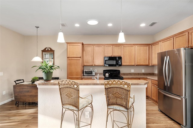 kitchen with pendant lighting, a center island with sink, black appliances, and light hardwood / wood-style floors