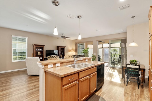 kitchen with dishwasher, a center island with sink, sink, hanging light fixtures, and light wood-type flooring