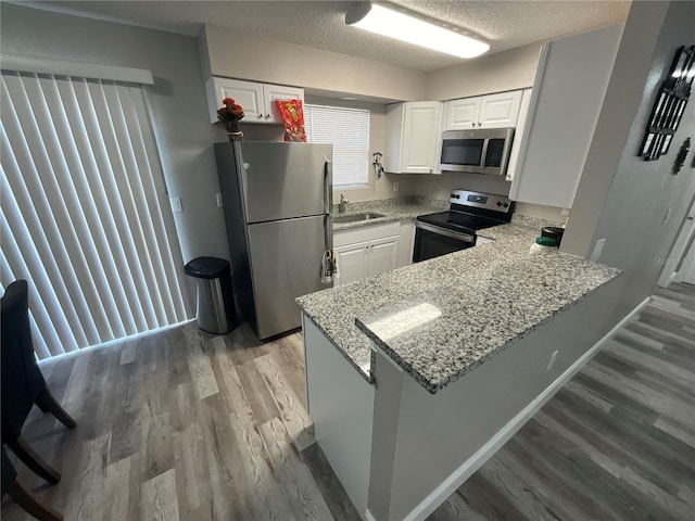 kitchen featuring kitchen peninsula, stainless steel appliances, white cabinets, and hardwood / wood-style flooring