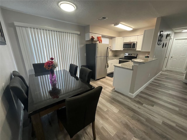 dining area with a textured ceiling and light hardwood / wood-style flooring