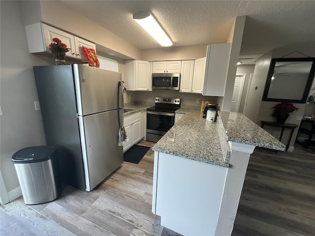 kitchen featuring stainless steel appliances, light stone counters, light hardwood / wood-style flooring, a textured ceiling, and white cabinets