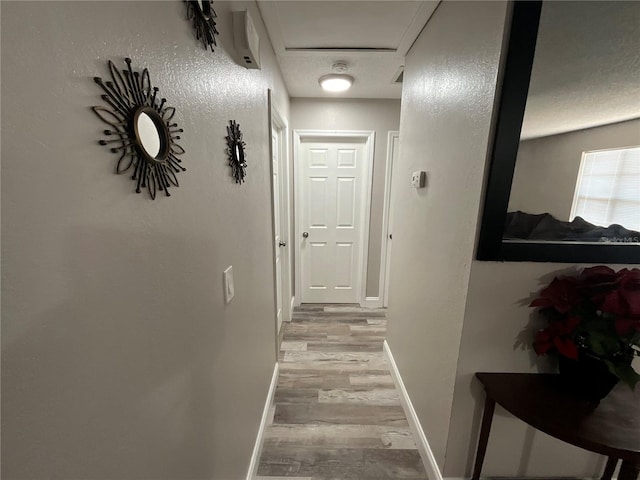 hallway with a textured ceiling and light hardwood / wood-style floors