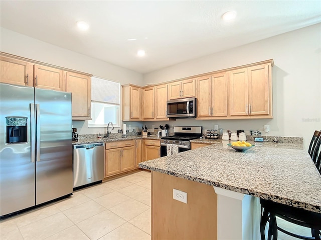 kitchen with kitchen peninsula, appliances with stainless steel finishes, sink, light brown cabinets, and a breakfast bar area