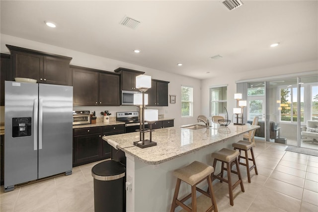 kitchen with sink, an island with sink, stainless steel appliances, and light tile patterned floors