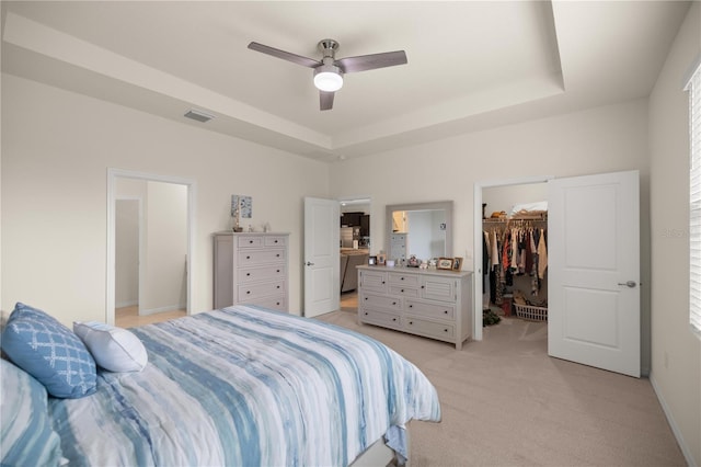 bedroom featuring ceiling fan, a raised ceiling, a walk in closet, light carpet, and a closet