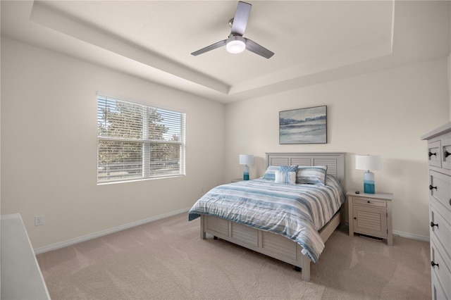 bedroom with light carpet, a raised ceiling, and ceiling fan