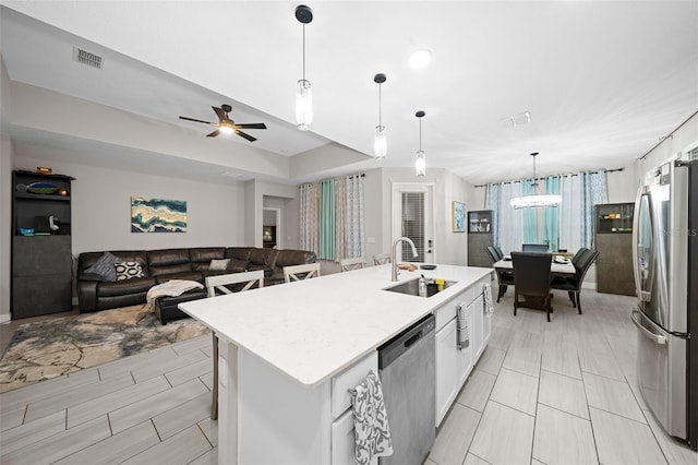 kitchen featuring stainless steel appliances, sink, pendant lighting, a center island with sink, and white cabinets