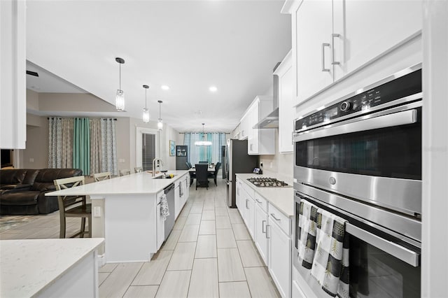 kitchen with hanging light fixtures, an island with sink, a kitchen bar, white cabinets, and appliances with stainless steel finishes