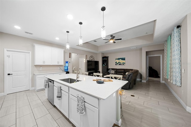 kitchen with stainless steel dishwasher, ceiling fan, sink, a center island with sink, and white cabinetry