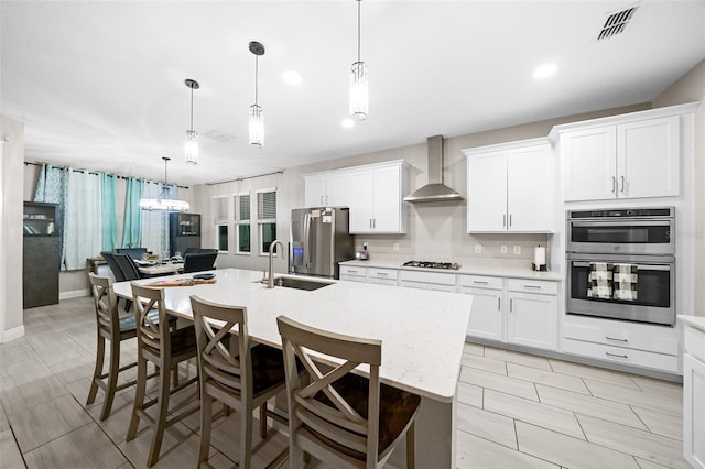 kitchen with a center island with sink, white cabinetry, wall chimney range hood, and stainless steel appliances