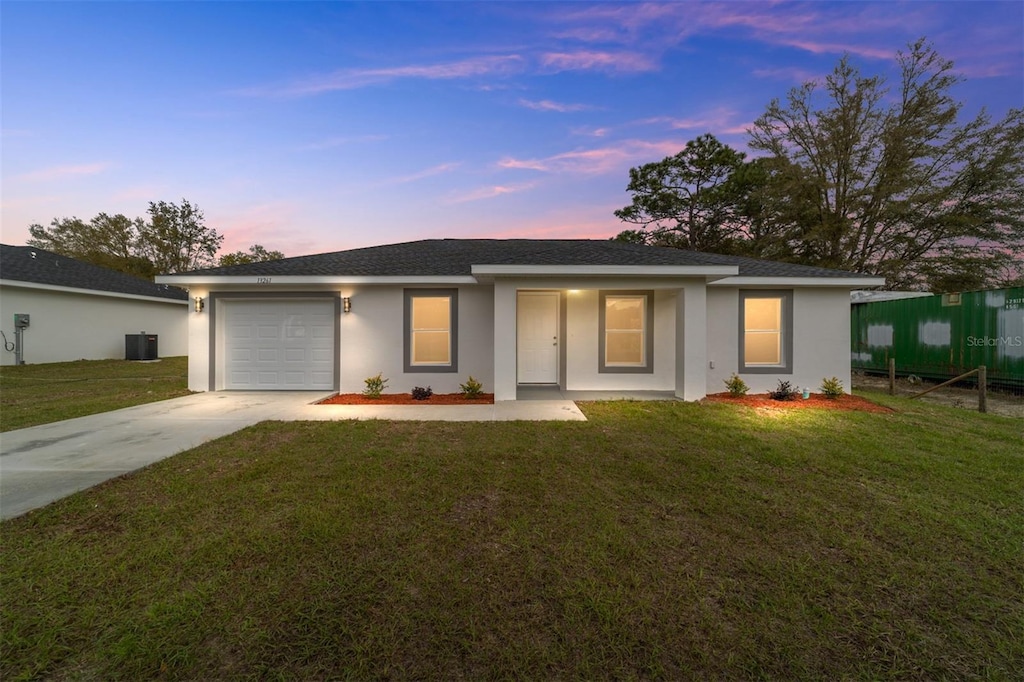 ranch-style house with a garage, central AC unit, and a lawn