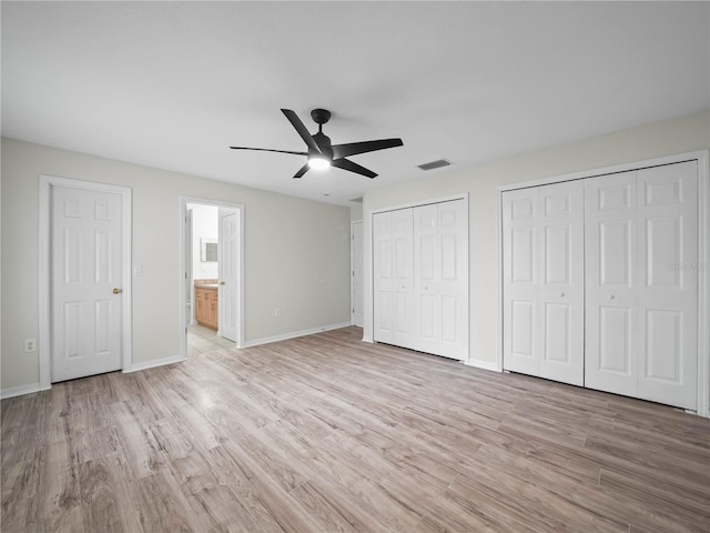 unfurnished bedroom with ceiling fan, light wood-type flooring, connected bathroom, and two closets