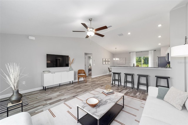 living room featuring ceiling fan with notable chandelier, light wood-type flooring, and vaulted ceiling