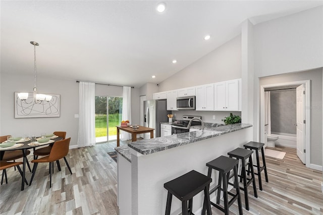 kitchen featuring kitchen peninsula, dark stone counters, stainless steel appliances, white cabinetry, and hanging light fixtures