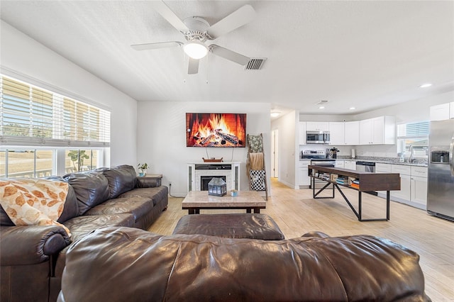 living room featuring a fireplace, ceiling fan, light hardwood / wood-style flooring, and plenty of natural light