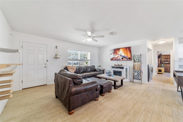 living room with ceiling fan, light wood-type flooring, a textured ceiling, and washer / clothes dryer